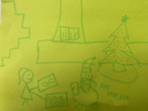 A little girl next to Santa holding cookies and a drawn picture, beside a Christmas tree and a large fireplace.