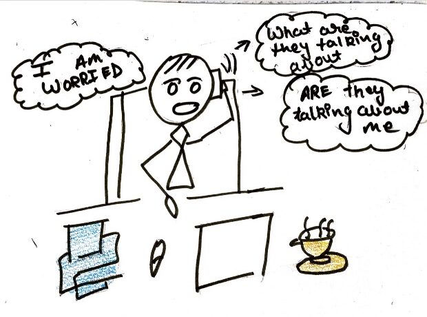 The stick figure in the image is sitting at his work place on a table and chair and looks very anxious and annoyed because he thinks that everybody are talking about him behind his back.